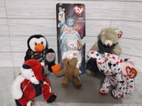 Four Beanie Baby plush toys in a line including two bears, a penguin, and a star-patterned dog. One bear is still packaged.