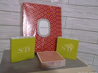 Two lime-green jewelry boxes with Stella & Dot branding and a red-orange patterned Stella & Dot gift bag or pouch behind.