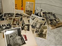 Large assortment of vintage black and white photographs along with some color slides, scattered on a surface with visible Kodak Photomechanical book underneath.