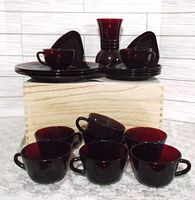 Cranberry glass cups, plates, triangular dishes and vase arranged on marble surface showing lot contents.