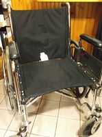 Front view of heavy duty wheelchair showing black fabric seat and backrest with chrome frame and leg rests