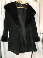 Full view of black leather jacket with faux fur collar and cuffs hanging on a hanger against a white backdrop.