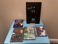 Set of 5 action movie DVDs displayed on blue tablecloth including Divergent, The Expatriate, Resident Evil Afterlife, The Matrix Revolutions, and Robocop, with a black sign behind them.