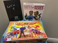 Two boxed Battle of the Sexes board games side by side, one unopened, one opened, shown with lot number sign