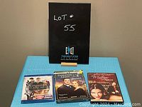 Lot with three DVDs: Kingsman The Secret Service, Downton Abbey Season 4, The Mistress of the Spices, arranged side by side on a blue surface, photographed from above.