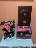 Photo showing the dragon phone and boxed ghost in cauldron decoration side-by-side on a blue surface against a wall with a lot number sign behind them.