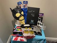 Photo of assorted Halloween and dress-up items showing a black and yellow cat-like mask, blue pom poms, various glasses including novelty and harlequin patterns, costume accessories like a vampire blood and fangs set, and a red inflatable guitar.