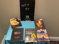 Five DVDs arranged on a blue surface showing titles: The Secret, The 300 Spartans, Mandelay, Riding Alone, plus one unidentified DVD.