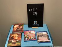 Four DVD/Blu-ray case covers on a blue cloth with a black sign behind reading Lot #34.