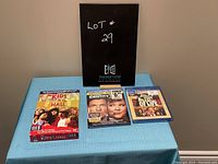 View of three DVDs displayed on a cloth-covered surface including Kids in the Hall, Identity Theft, and Monty Python The Meaning of Life.