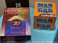 Photo showing Pictionary 20th Anniversary Edition game box with pencil design and Mad Gab adult party game box.