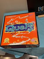 Top view of the bright orange Quelf game box showing the colorful and whimsical game title and illustrations.