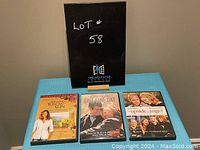 Three romantic DVDs including Under the Tuscan Sun, One Fine Day, and The Upside of Anger, displayed on a table with a black sign behind.