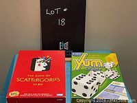 Photo showing two boxed board games, Scattergories in red box and Yum Poker in green and yellow box, on a blue cloth surface.