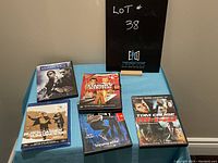 Five DVDs arranged on a blue tablecloth under a black sign with lot number 38. DVDs include Miami Vice, Starsky & Hutch, Butch Cassidy & the Sundance Kid, and Mission Impossible 3.