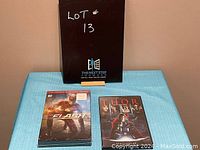Photo showing The Flash Complete Second Season DVD in shrink wrap and Thor Blu-ray case placed on blue cloth with black box in background.