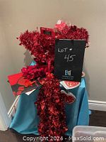Lot of assorted Valentine's Day themed decorations including red glittery tinsel garland, heart-shaped paper plates or signs, plastic novelty items, and cards displayed on a blue draped surface.