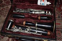 Clarinet dismantled in a maroon velvet-lined storage case with a bottle of bore oil.