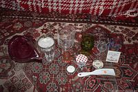 Photo showing all the miscellaneous glass items laid out on a patterned surface including the red glass cornucopia, various drinking glasses, small containers, and a ceramic dish with lid.