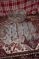 Photo showing the large crystal punch bowl surrounded by 20 matching serving cups arranged on a patterned rug.
