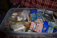 Plastic bin filled with boxed and loose incandescent light bulbs, packaging, and some hardware pieces.