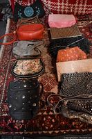 Photo showing 13 assorted shoulder and evening bags in various materials and colors arranged on a patterned rug.