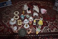 Wide view of assorted porcelain mini tea set pieces, various porcelain figurines, and small decorative items arranged on a patterned carpet.