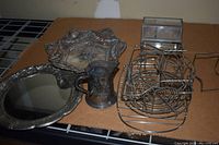 Top down overhead image of silver trays, small creamer, metal plate stand and glass box displayed on cardboard surface