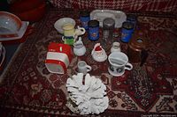 Overview of assorted household and decorative ceramic items, coffee mugs, coral, and tin cups on patterned rug.