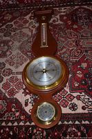 Full view of vintage wall mount barometer, thermometer, and hygrometer on a patterned carpet.