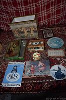 Photo of vintage decorative items including a footed box with horse race scene, various tins, sewing kit, plaques, framed art, and an advertisement plaque.