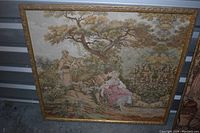 Full view of the vintage tapestry in a gold gilded frame showing a romantic couple under a tree and classical garden elements.