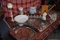 Wide view of all items on a red patterned carpet, including serving trays, bowl, coat rack, owl, lamp and small figurines