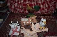 The entire set of five porcelain figurines and planters on a patterned carpet with a red and white backdrop.