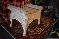 White wicker bench on patterned carpet with a red and white plaid backdrop. Shows full front and side view of bench and its construction.