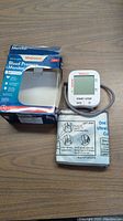 Blood pressure monitor with attached cuff and original Walgreens box on a wooden surface.