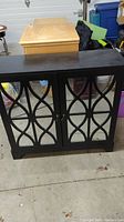 Front view of black wooden cabinet with glass paneled doors, decorative lattice design over glass, and round knobs.