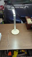 Full view of lamp on desk showing slim adjustable arm, rectangular light head, and power cable.