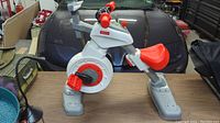 Side view showing the stationary bike with red pedals and adjustable red seat on white and gray frame.