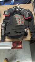 Full body view of black EVS Comp Suit ballistic jersey including chest protector, shoulder and elbow guards, hung on hanger on table.