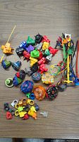 Beyblade tops, ripcords, launchers, and various parts spread out on wooden surface.