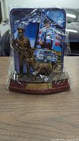 Photo of K-9 Police Unit sign figurine in plastic wrapping showing police officer and K-9 dog in bronze color against background of police imagery