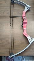 Full view of the kids compound bow showing pink central riser and silver limbs with bowstring attached.