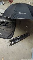 Black Calumet photo studio umbrella open showing logo; laid on floor with carrying bag and tripod parts