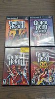 Four PlayStation 2 Guitar Hero game cases arranged in a square on a wooden surface.