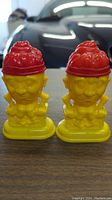 Photo showing a front view of the pair of yellow Humpty Dumpty salt and pepper shakers with red hats on a wooden surface.