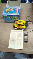 Photo showing the yellow wire-controlled Wheelie Bug toy car, its original colorful box with images, the wire controller, and the instruction sheet on a wooden table.