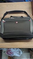Front view of black Wenger laptop bag on table showing logo and zipper compartments.