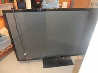 Front view of older model 60 inch Samsung television with black bezel and power cord draped over screen, positioned on stand.