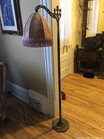 Full view of antique bridge lamp with pink and tan floral fabric shade with fringe, tall brass metal base with curved arm.